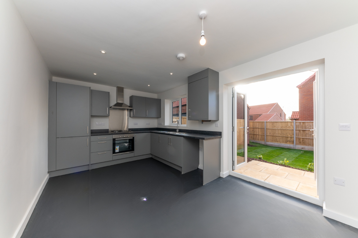 Kitchen diner with open french doors out on to a turfed lawn with the sun shining