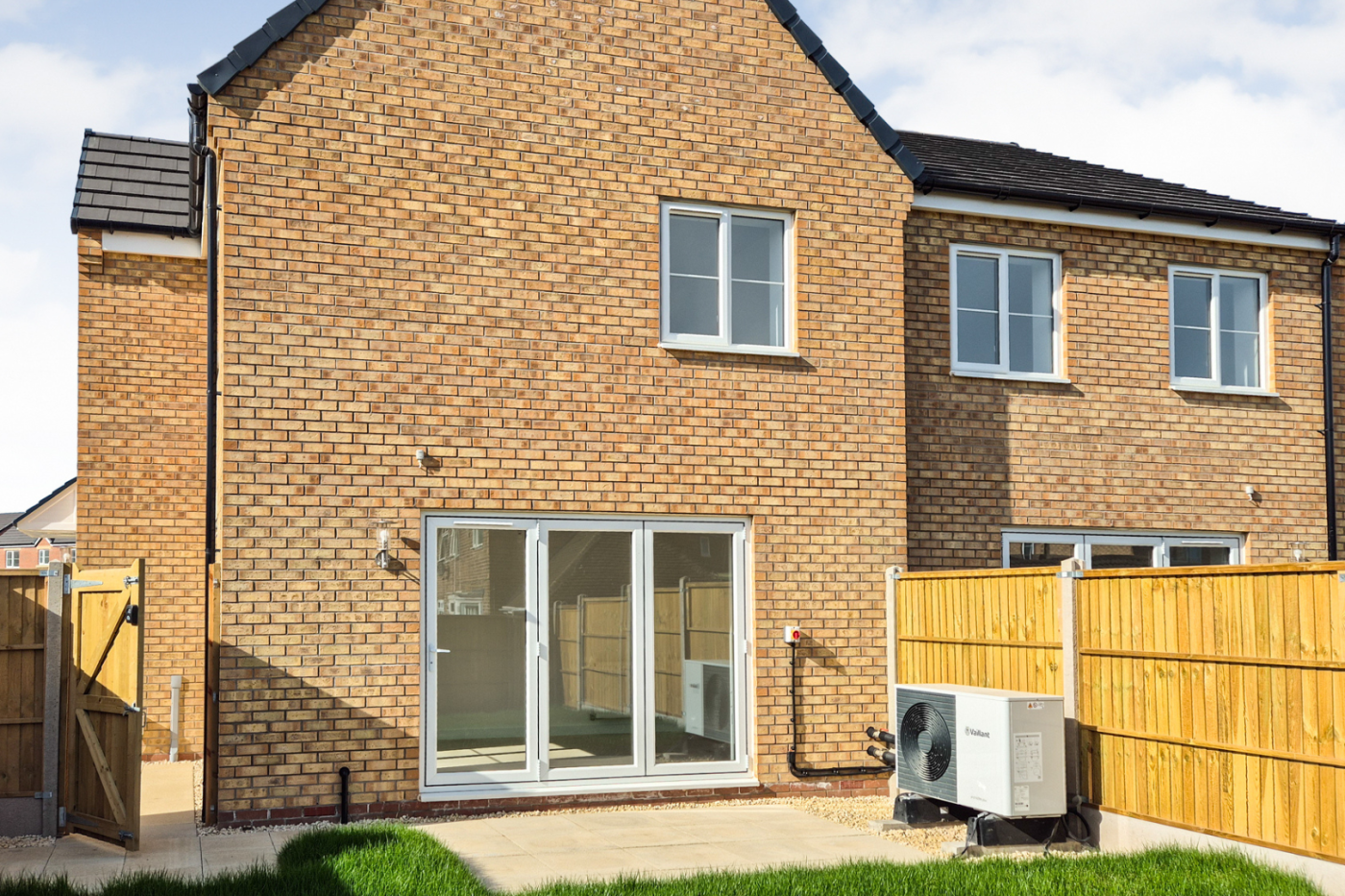 A view of the back of the house showing patio, the fence, the gate and  bi fold doors leading to the kitchen