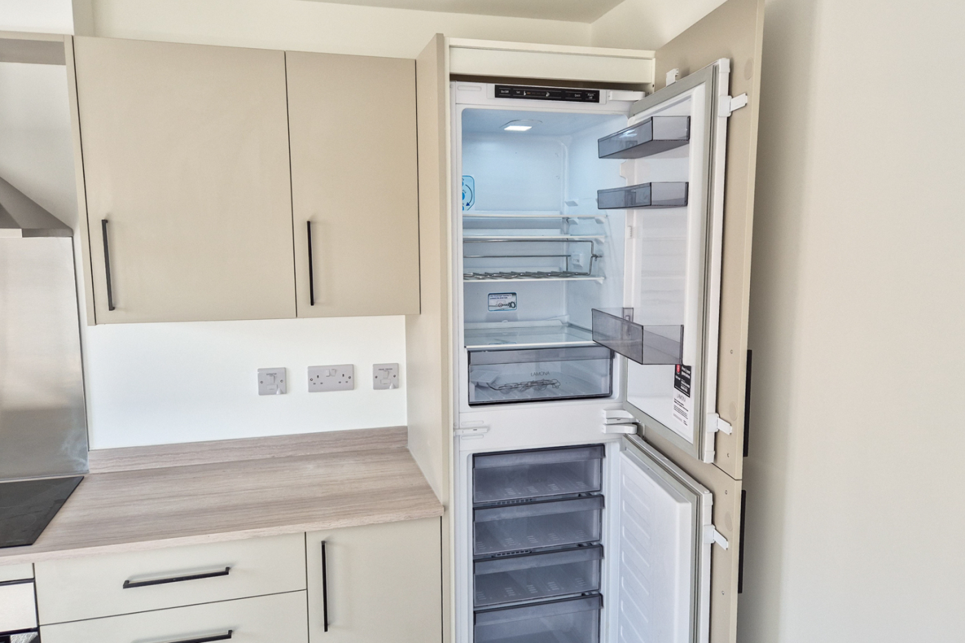 The kitchen showing the integrated fridge freezer which is open and in the right hand corner with the kitchen worktop and hob to the left of it.