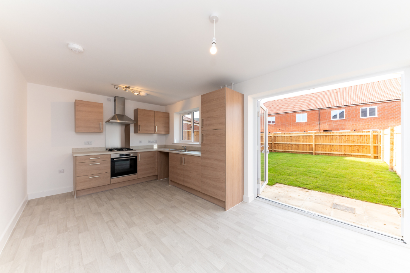 Kitchen diner with open french doors out on to a turfed lawn with the sun shining