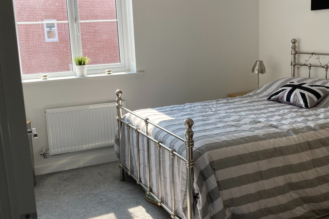 A photo of a second bedroom with a light grey carpet showing a bed and windows