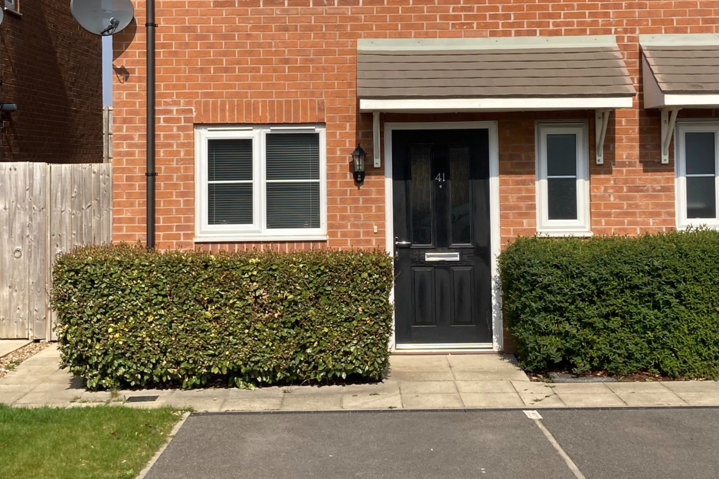 A picture of the front of the house showing a black door, a parking space and a hedge