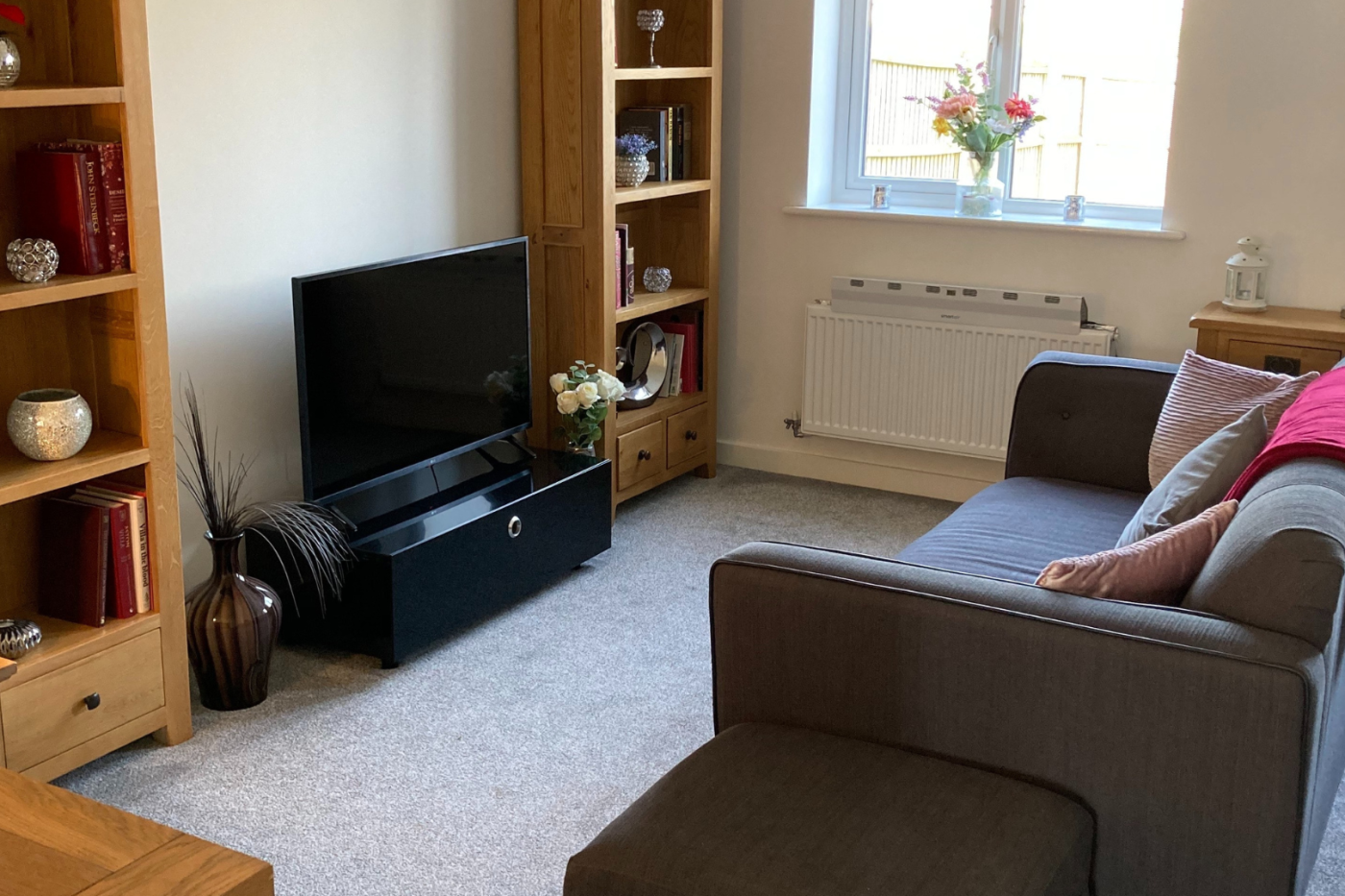 A picture of the front room showing a softa, tv, furniture, radiator, and windows