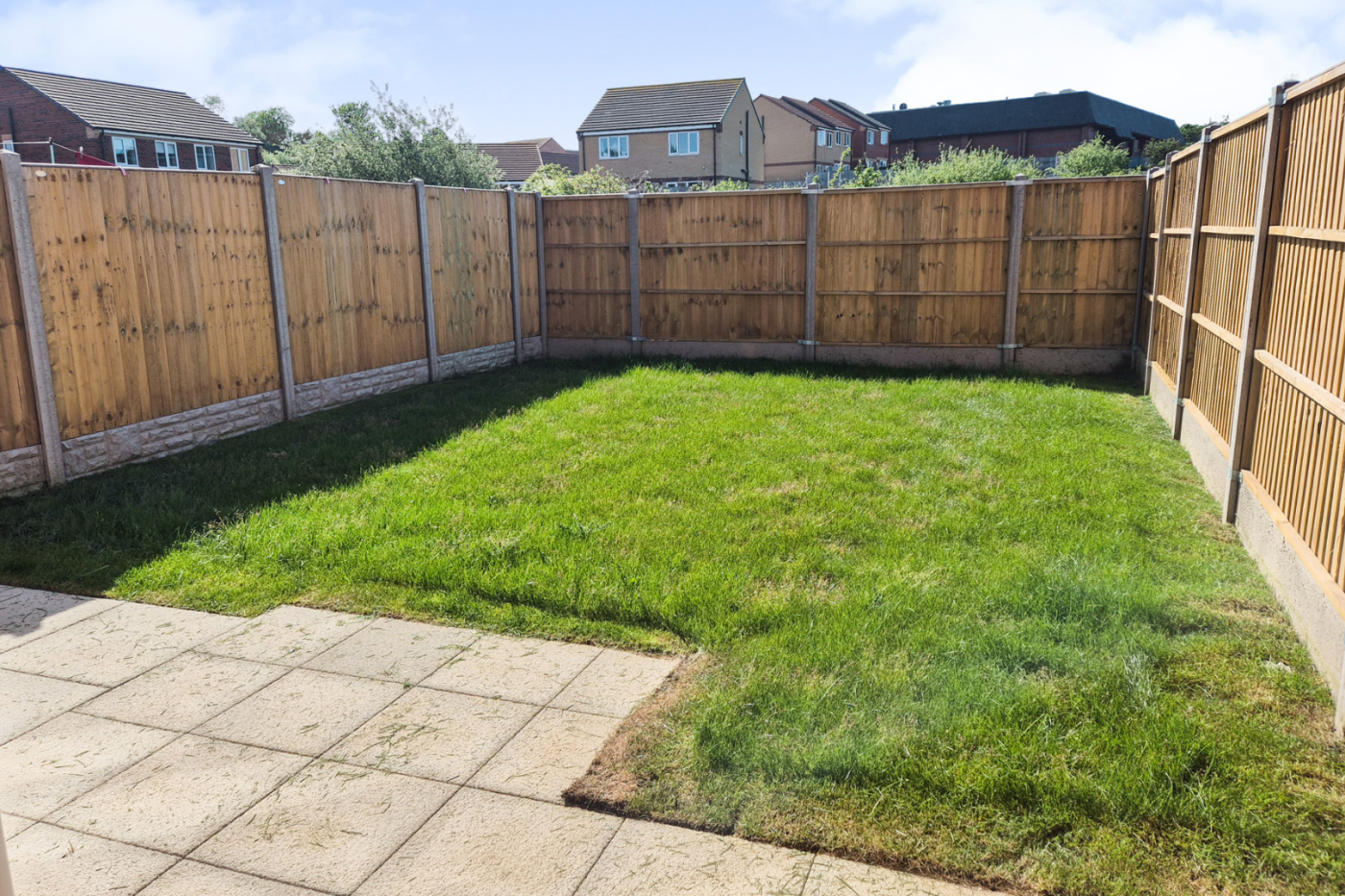 The garden showing patio, green grass and fences on three sides