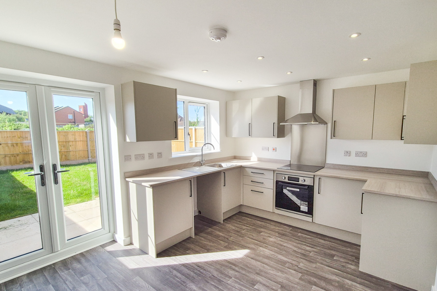 The kitchen showing the kitchen worktop, cupboards, built in hob and cooker, and two doors leading to the back garden