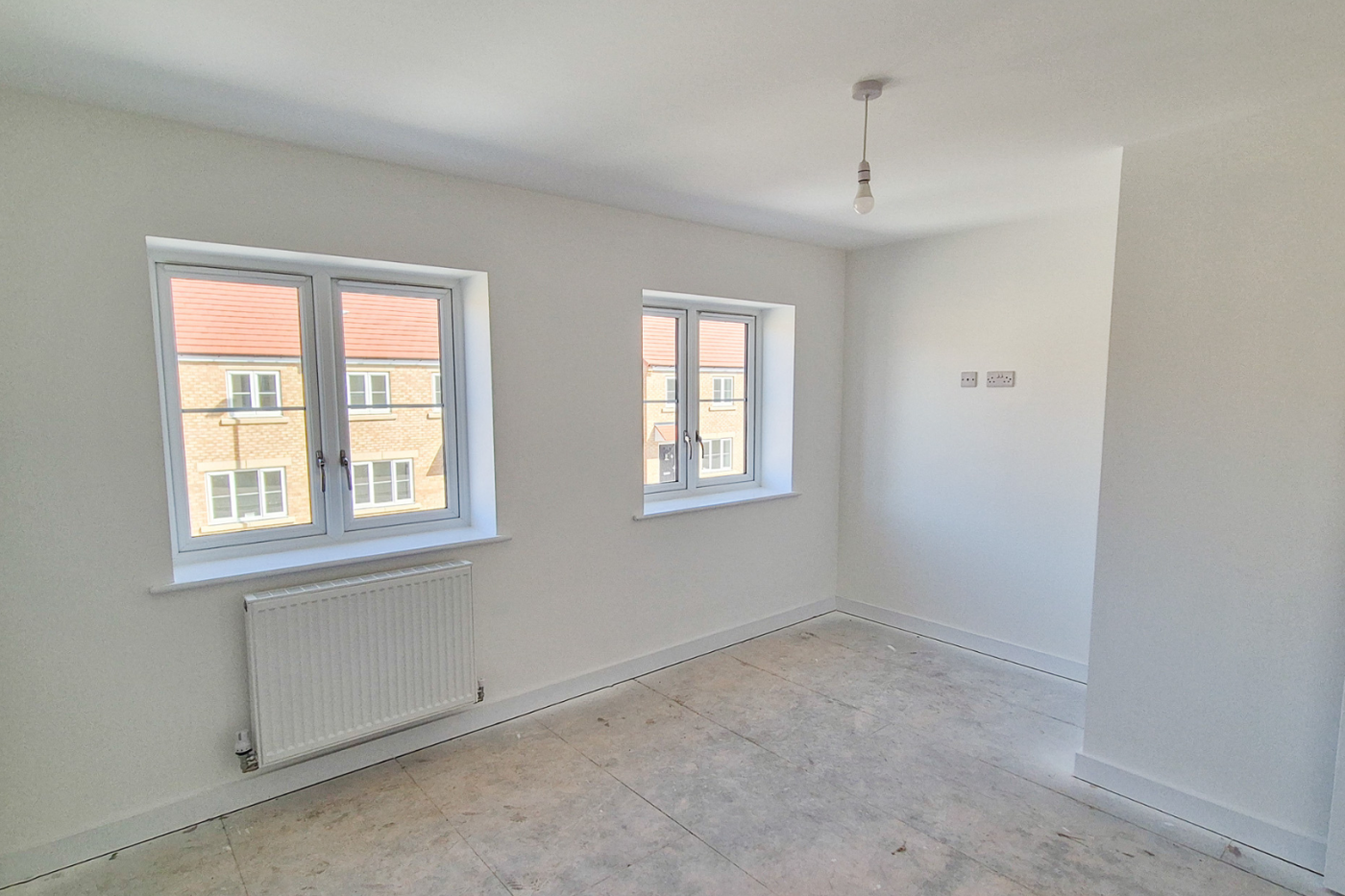 A bedroom with two windows, a radiator and plug sockets a third of the way up the wall