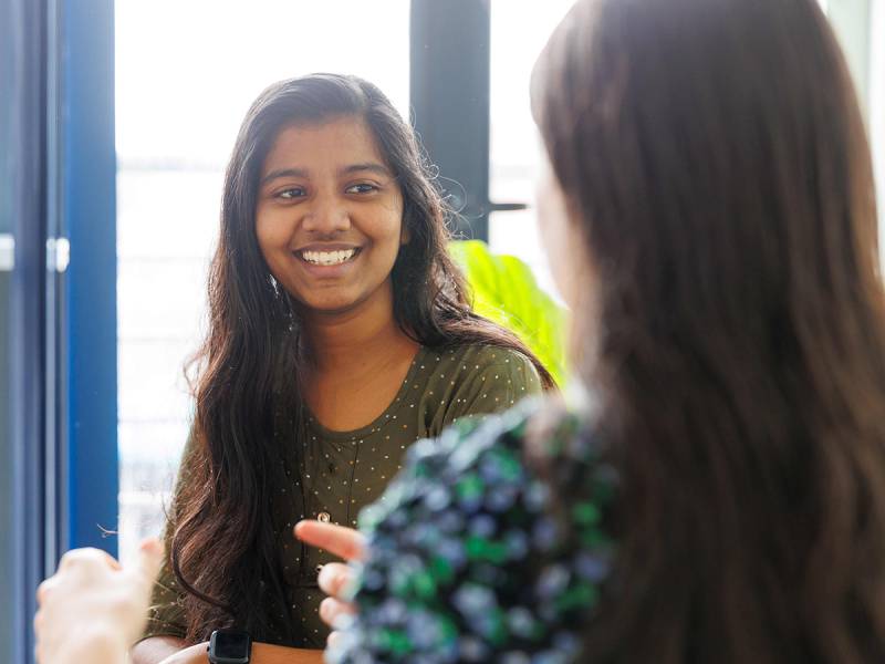 Two women chatting and smiling in front of a window