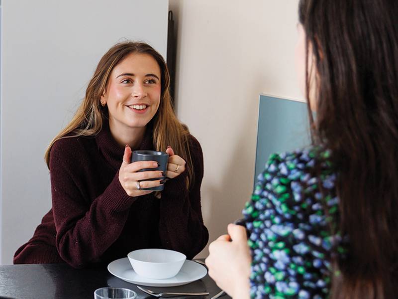 Two women chatting smiling in kitchen with cup of tea