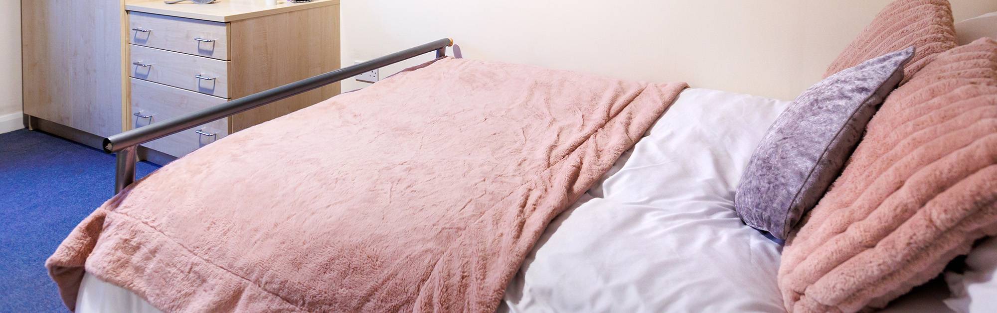 Close up of bed with pink cushions and blanket