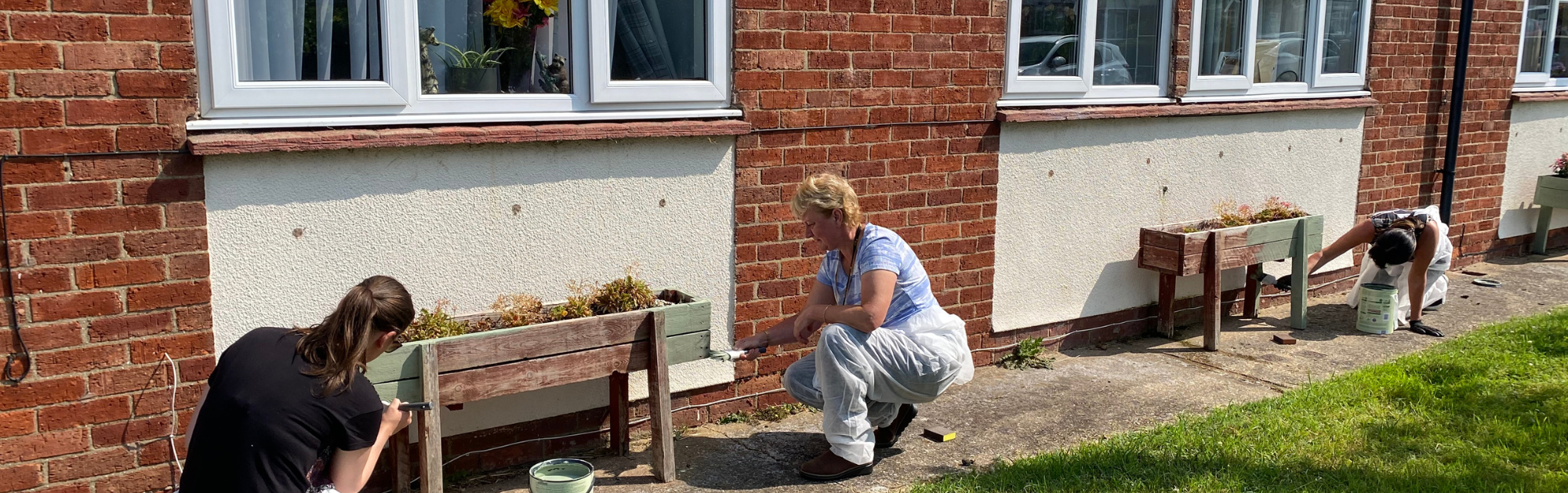 Three people painting flower pots in the sunshine