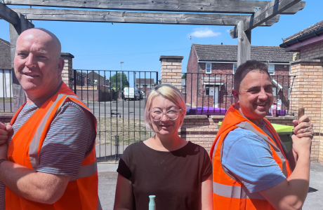 Two men in high vis and a woman stand with brushes at a volunteer day
