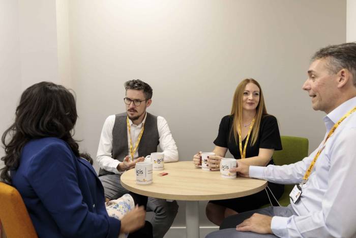 4 acis group employees sitting talking around a table