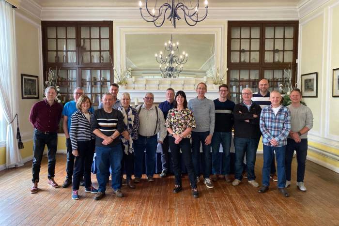 Group of 15 people standing in a large room with chandelier above them