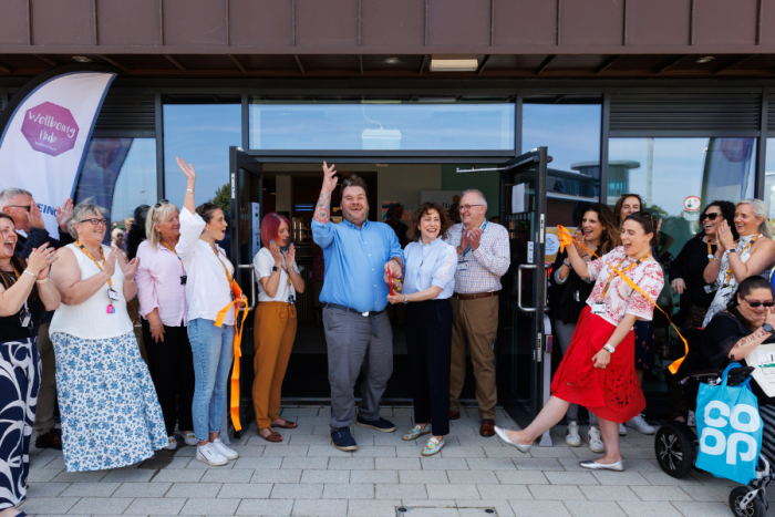 A group of people watching a man and woman cut a ribbon in front of a building