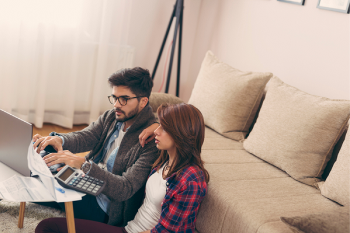 A couple sat on the floor looking at bills and a laptop
