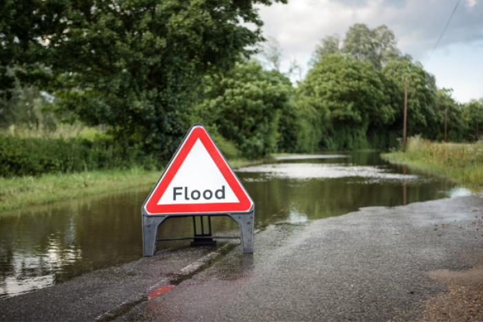 An image of a flooded road with a triangle flood sign.