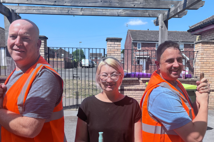 Two men in high vis and a woman stand with brushes at a volunteer day