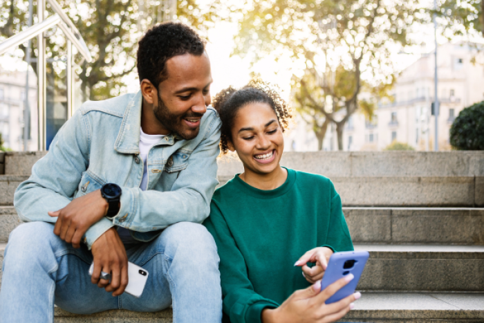 Two people sat on some steps looking at a phone and smiling