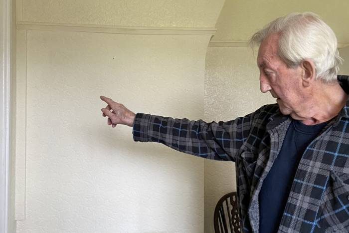 Elderly man pointing at cream wall