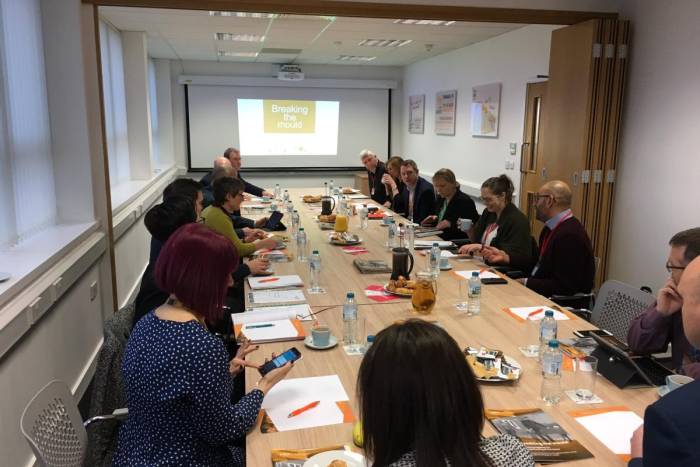 Large boardroom with many people sitting around a table with projector presentation