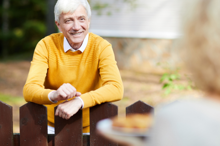 Elderly man leaning on gate.