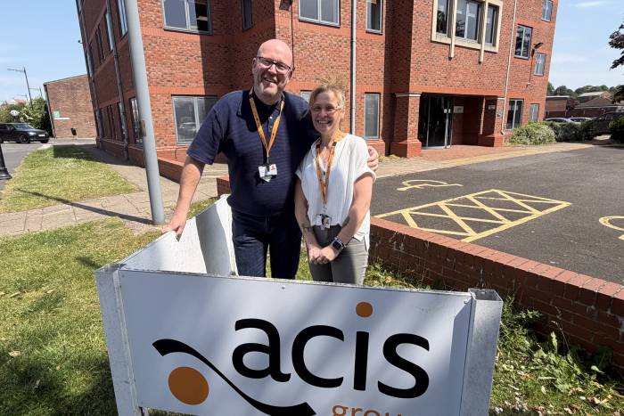A man and woman stand side by side outside Acis Group's business office