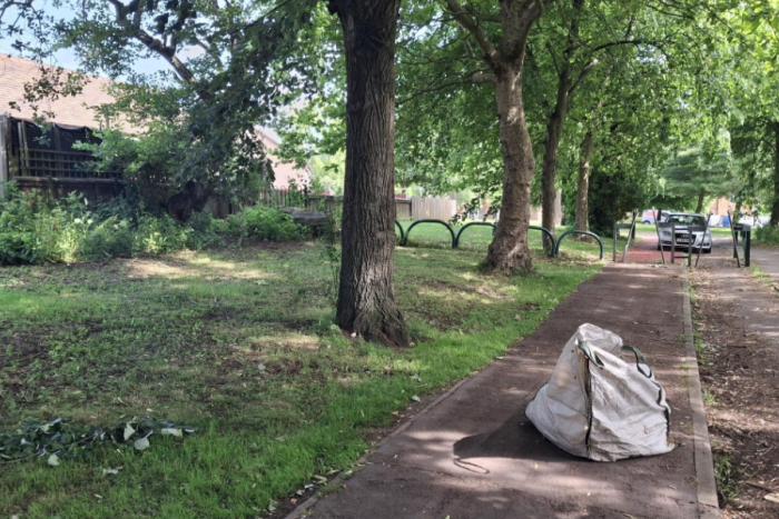 Some trees, freshly cut grass and clean pavements with a white bag of overgrow on the pavement 