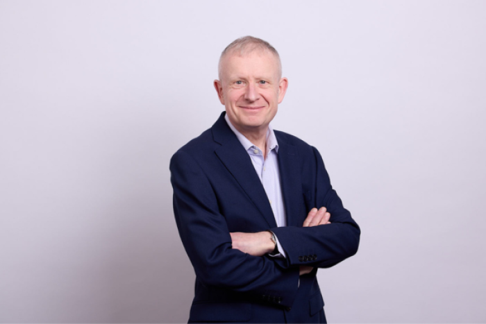A man in a shirt and jacket smiling with his arms crossed