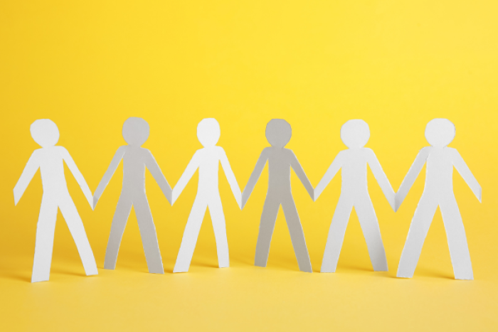 A picture of paper cut outs of people holding hands on a yellow background