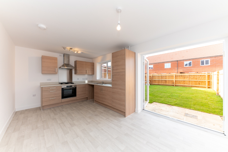 Kitchen diner with open french doors out on to a turfed lawn with the sun shining