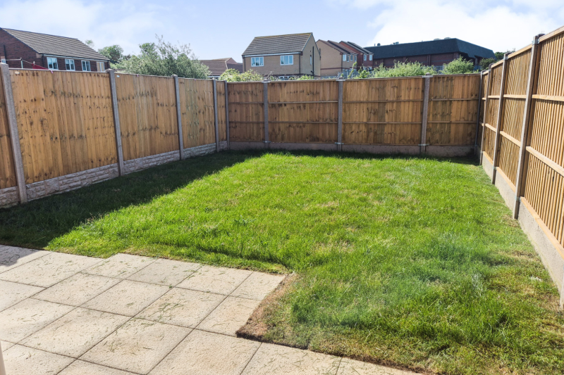 The garden showing patio, green grass and fences on three sides