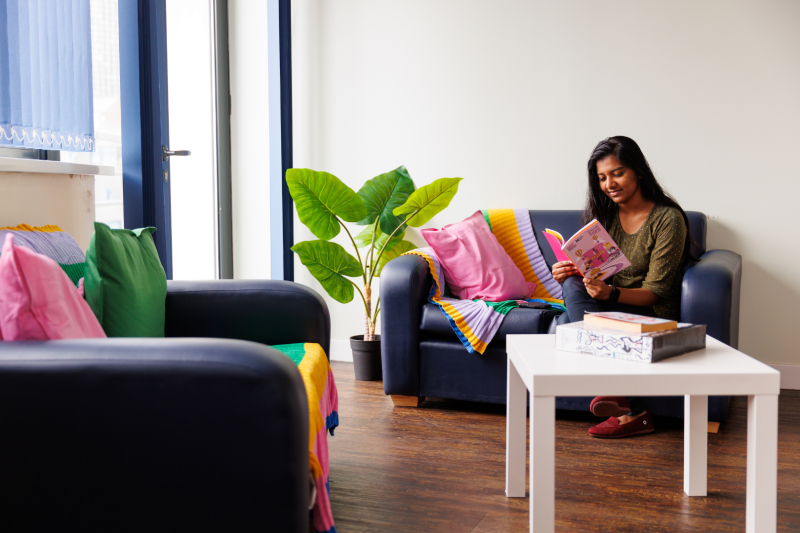 Female student sitting on sofa reading a book