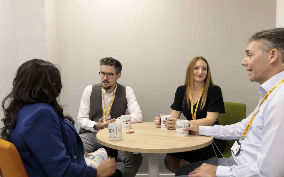 4 acis group employees sitting talking around a table