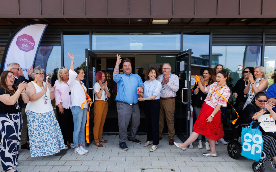 A group of people watching a man and woman cut a ribbon in front of a building
