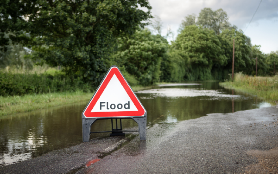 An image of a flooded road with a triangle flood sign.