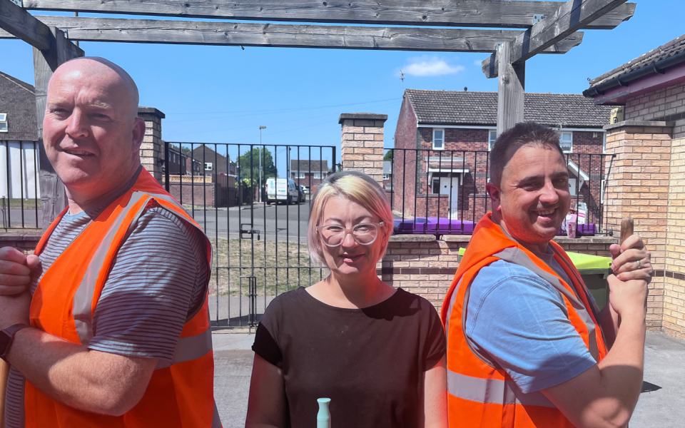 Two men in high vis and a woman stand with brushes at a volunteer day