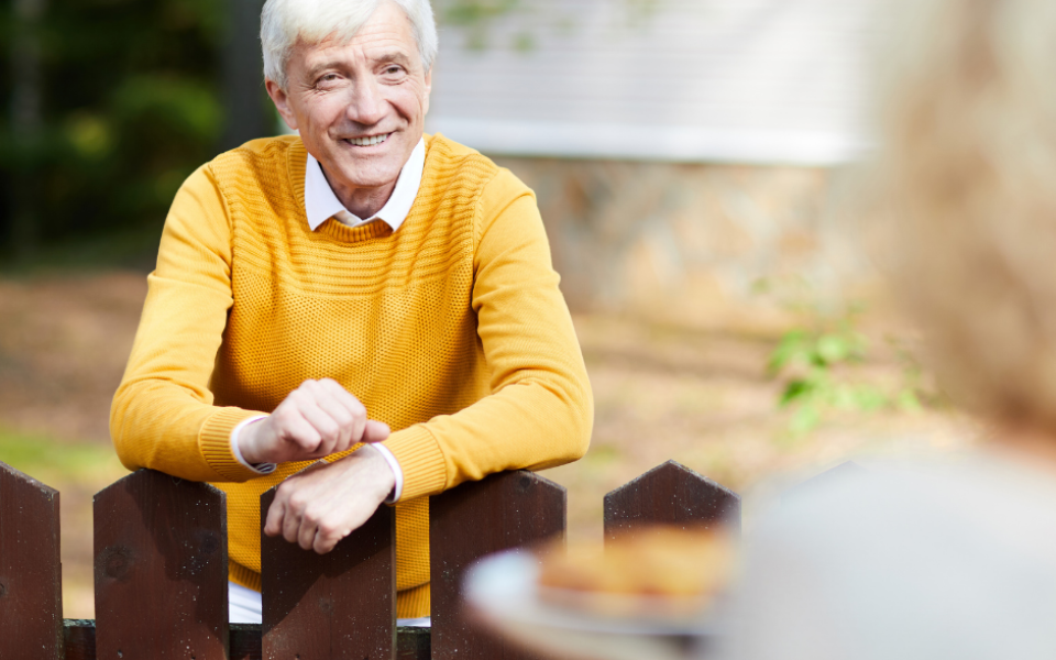 Elderly man leaning on gate.