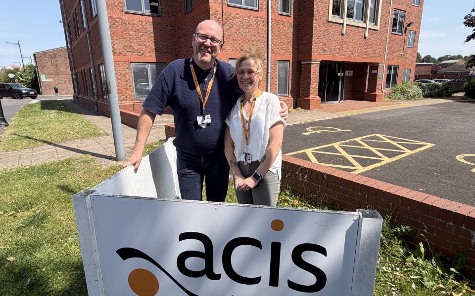 A man and woman stand side by side outside Acis Group's business office