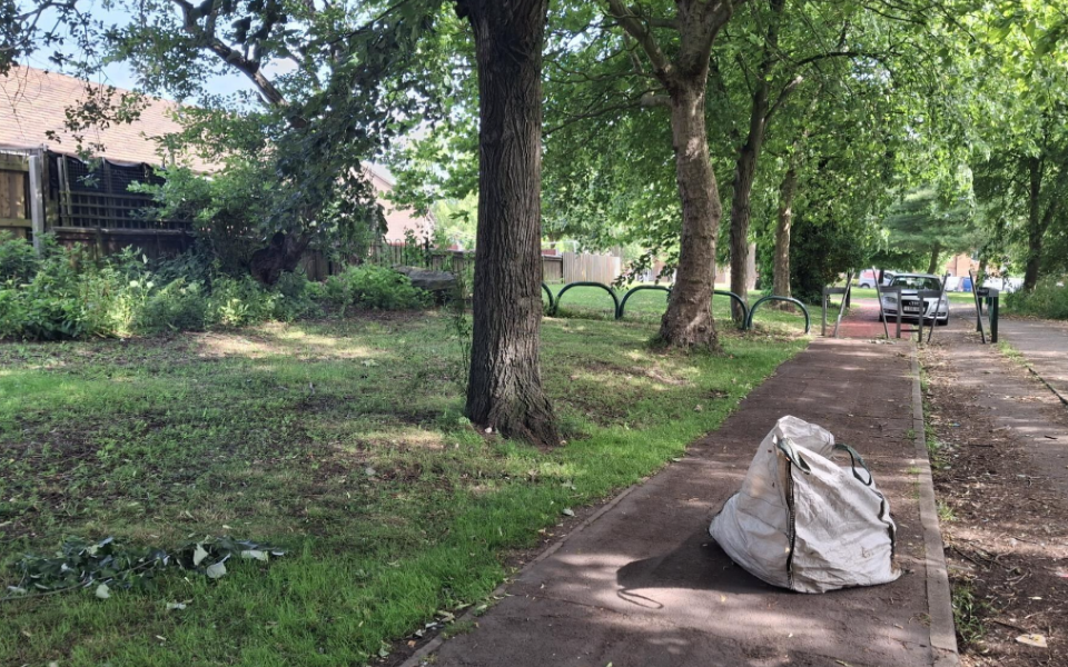 Some trees, freshly cut grass and clean pavements with a white bag of overgrow on the pavement 