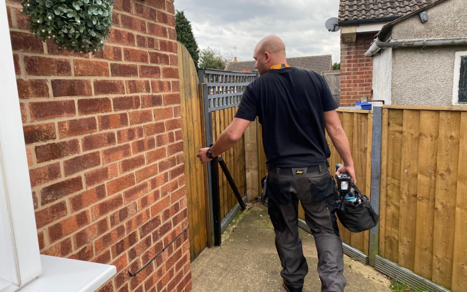 Trade worker opening gate carrying tool bag