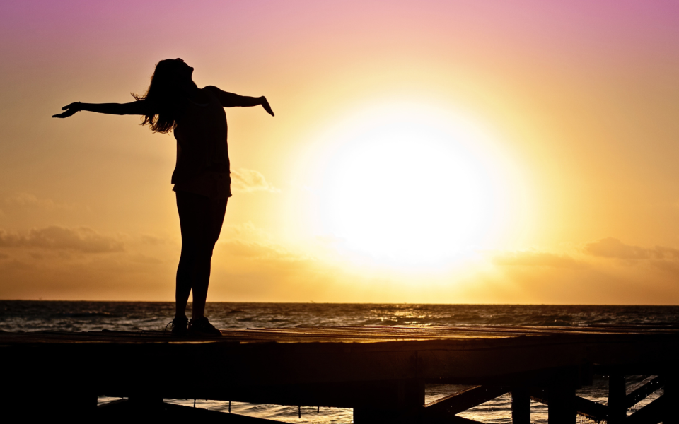 Person standing with arms out in front of sunset